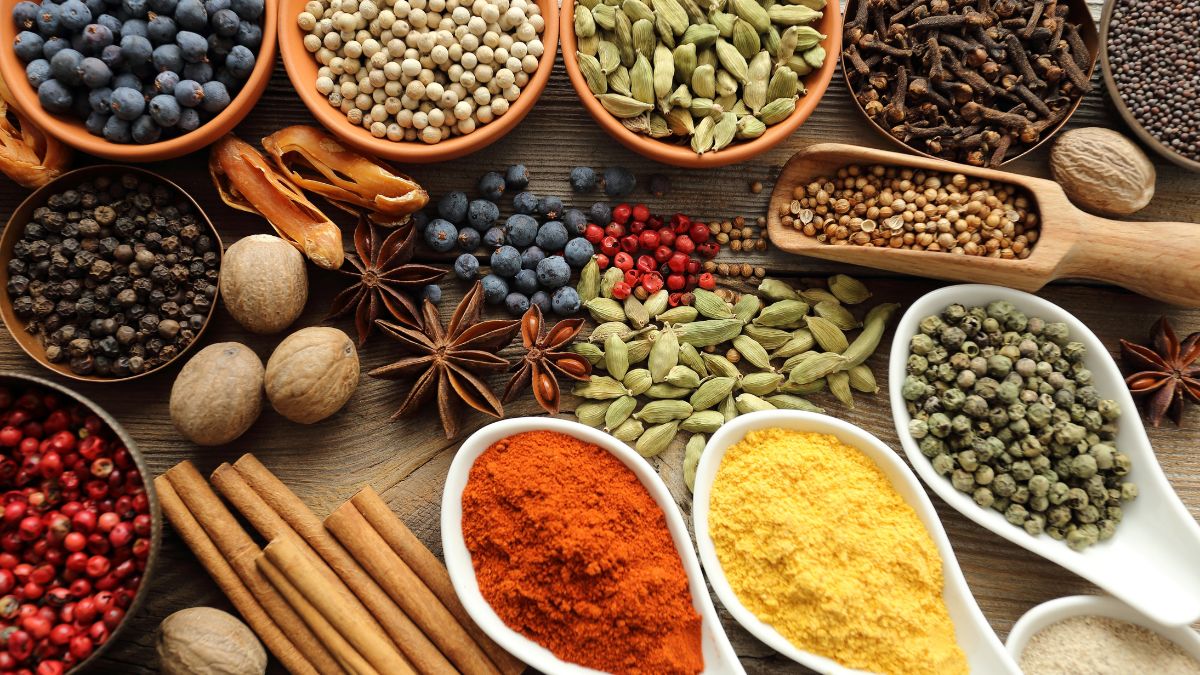 Assorted whole and ground spices in bowls and spoons on rustic table.