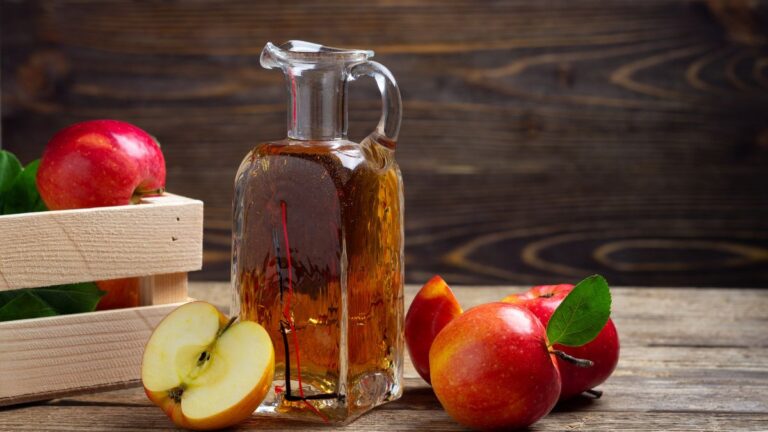 Bottle of apple cider vinegar with fresh apples on table.