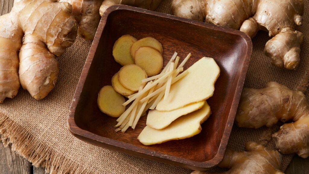 Fresh ginger root and slices on a wooden board.
