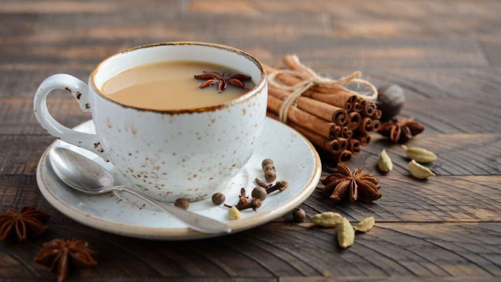 Cup of chai tea with cinnamon, cardamom, and star anise on table.