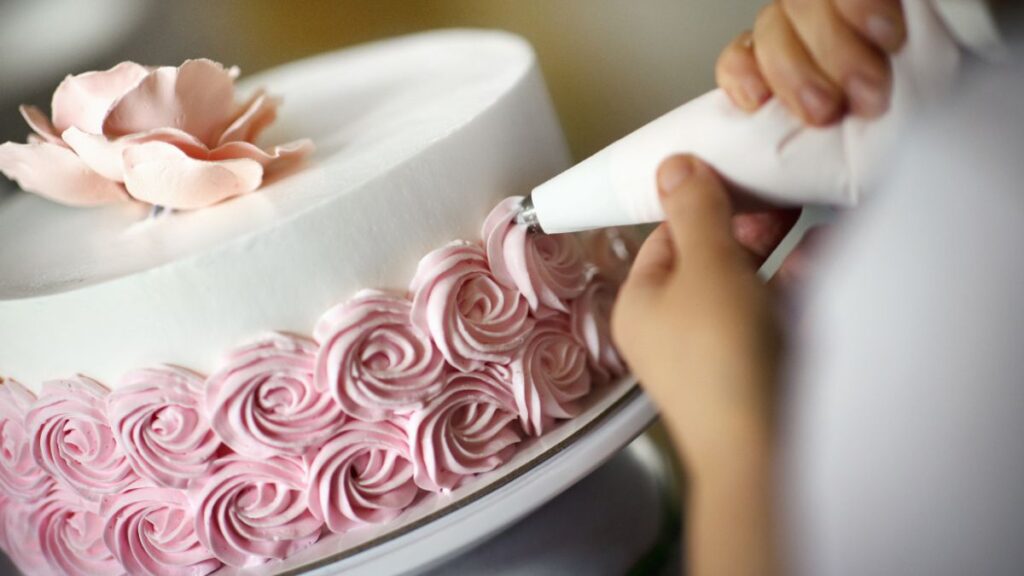 Piping pink rosettes onto a frosted white cake for a homemade finish.
