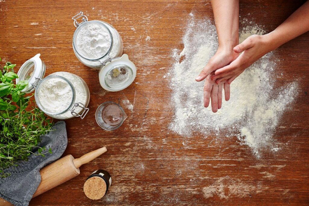 Flour in a jar and wooden surface with hands working.