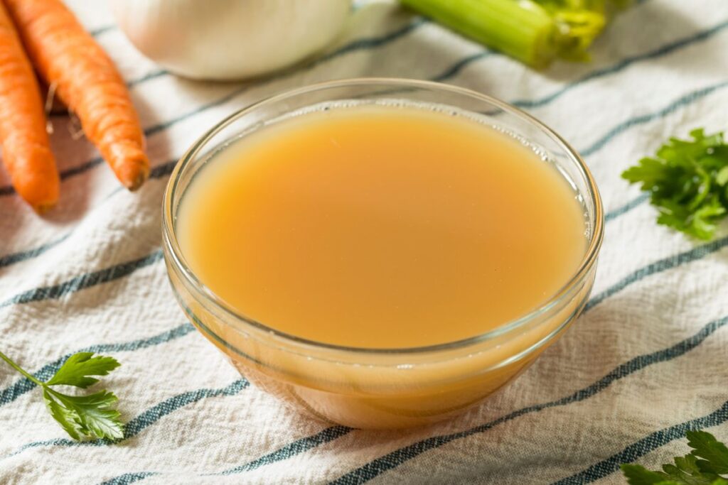 A bowl of vegetable broth with veggies in the background.