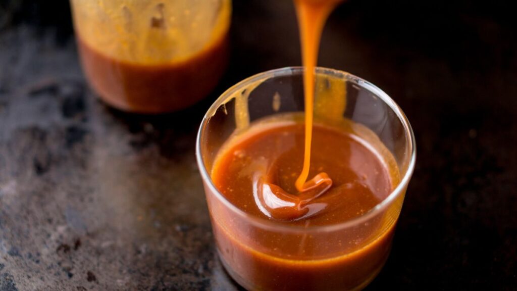 Glass cup of golden caramel sauce being poured in a swirl.