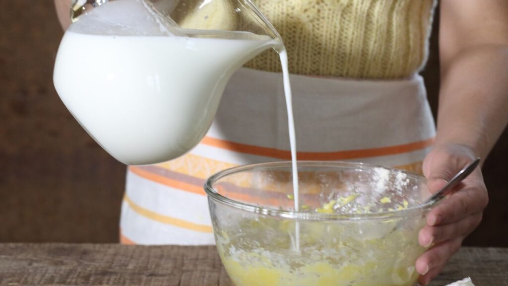 Pouring milk into a glass bowl of cake batter to replace water in boxed mix.