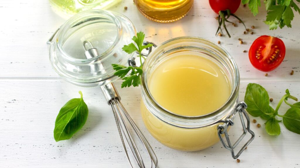 Small glass jar of apple cider vinegar salad dressing with spoon.