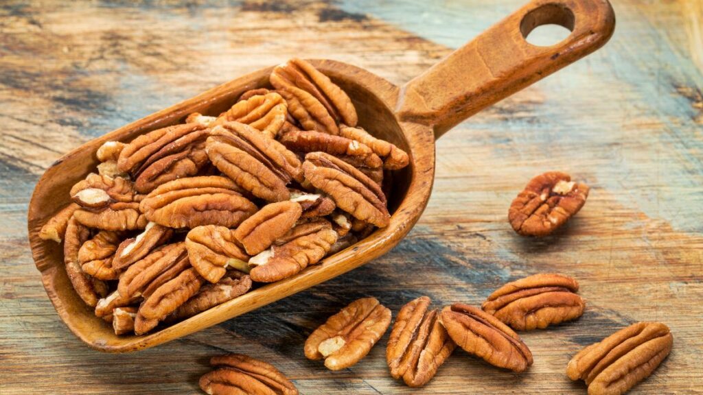 Rustic wooden scoop filled with pecans on a wooden table.