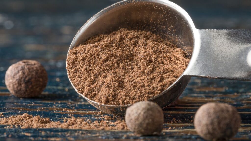 Ground allspice powder spilling from measuring spoon beside whole allspice berries.