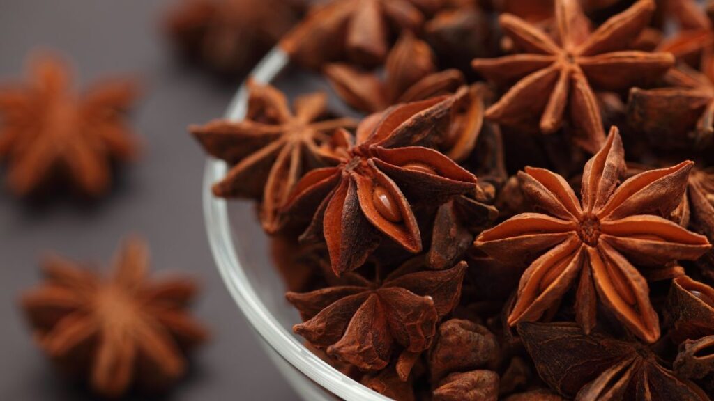 Star anise pods in a glass bowl with rustic background.