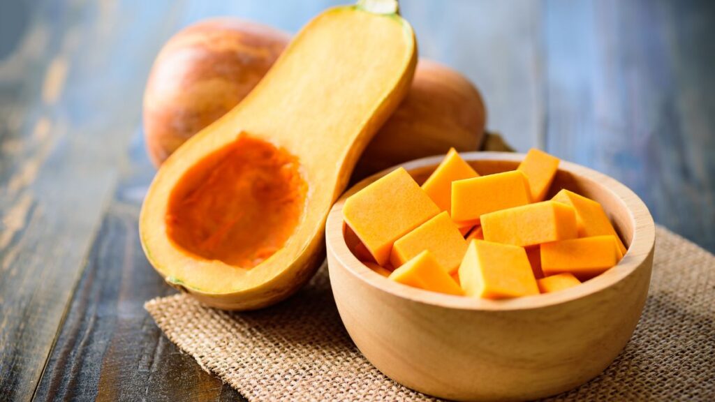 Wooden bowl of cubed butternut squash beside a halved squash.