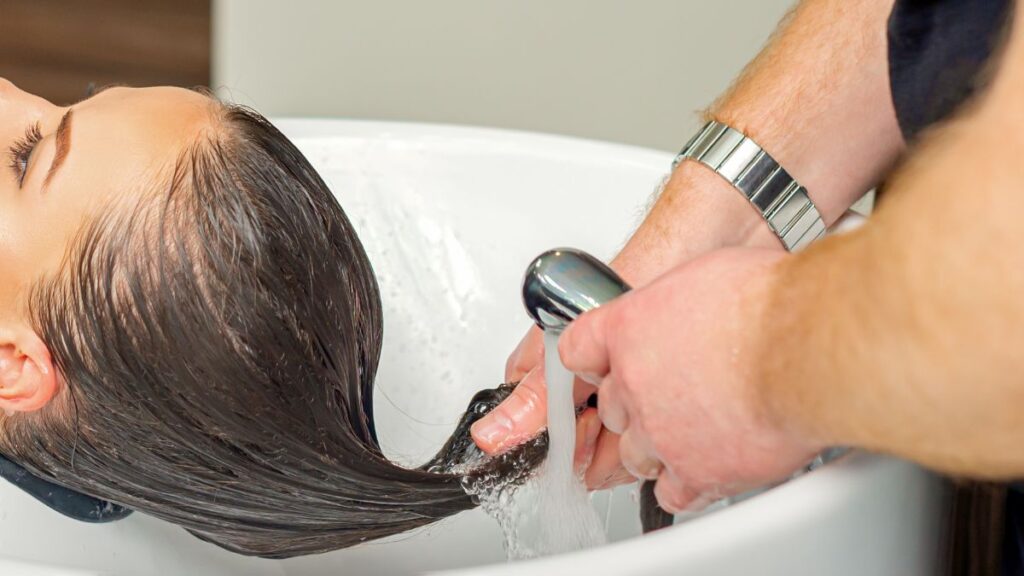 Clear bottle of apple cider vinegar hair rinse beside wooden brush.