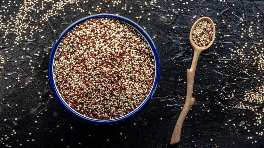 Quinoa in a bowl and a spoon placed on a black surface.