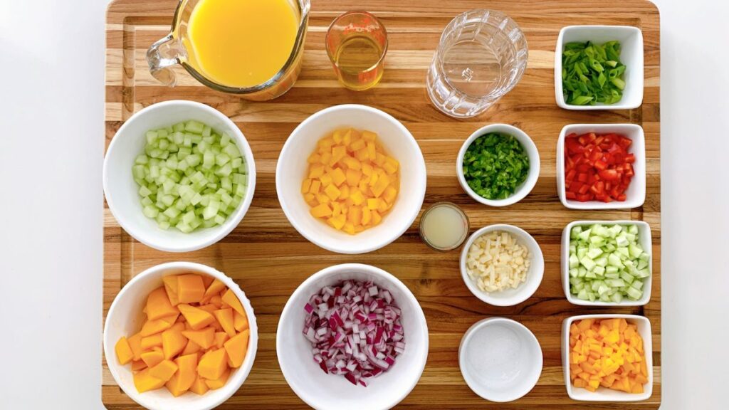 Cutting board with bowls of chopped vegetables, herbs, and liquids prepped for cooking.