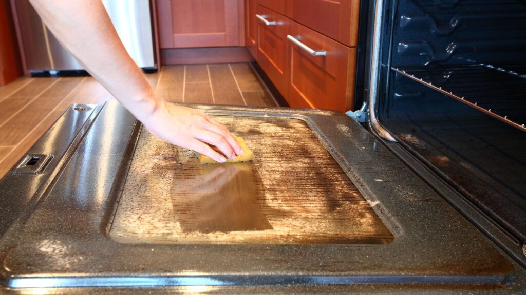 Scrubbing oven surface clean with baking soda paste.