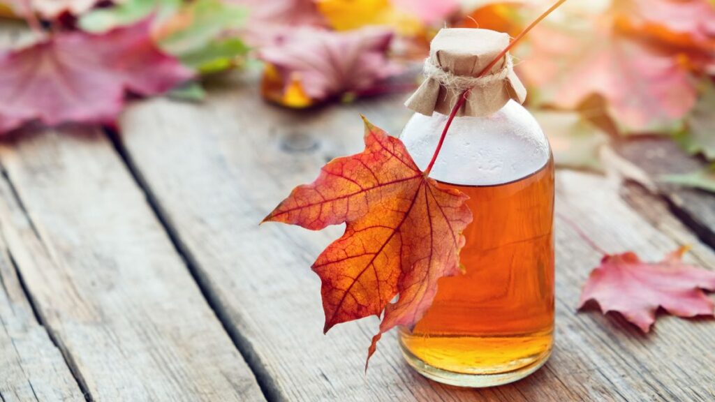 Bottle of maple syrup decorated with autumn leaf on rustic wood.