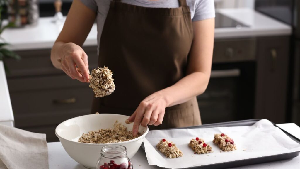 Woman shaping homemade oat and cranberry granola bars on a baking sheet.