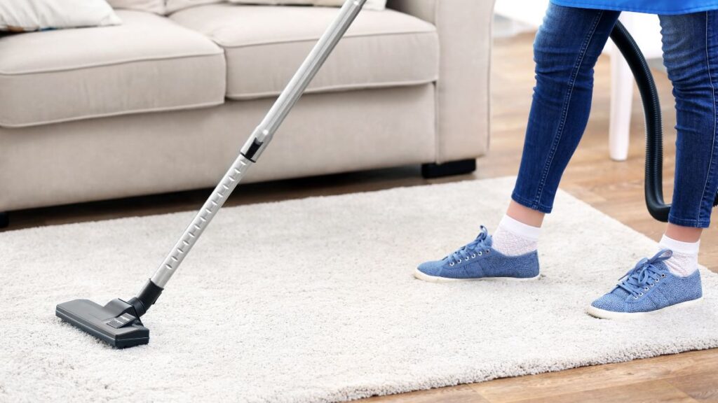 Vacuuming carpet after sprinkling baking soda for deep clean.