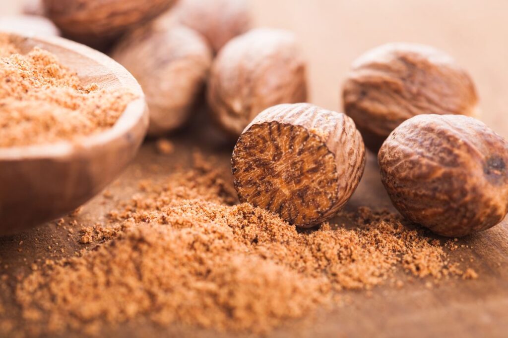 Ground and whole nutmeg on a wooden surface.