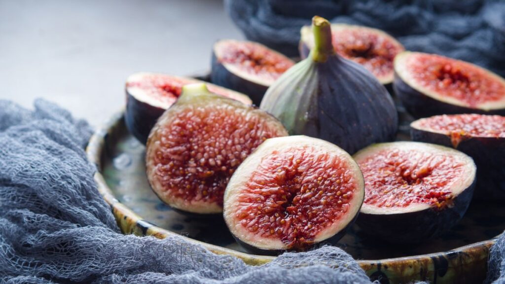 Halved figs with ruby centers on rustic plate and fabric background.