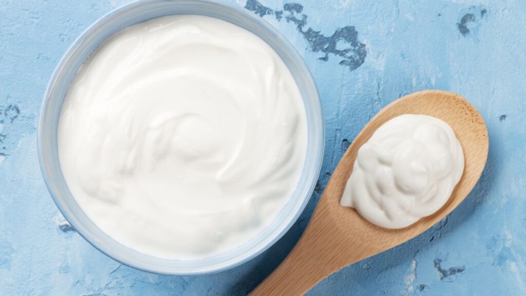 Bowl and spoon filled with sour cream on a blue background.