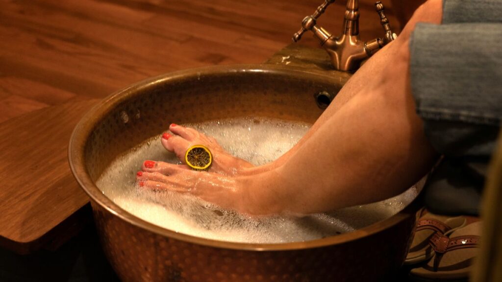 Wooden bowl with warm apple cider vinegar foot soak and towel.
