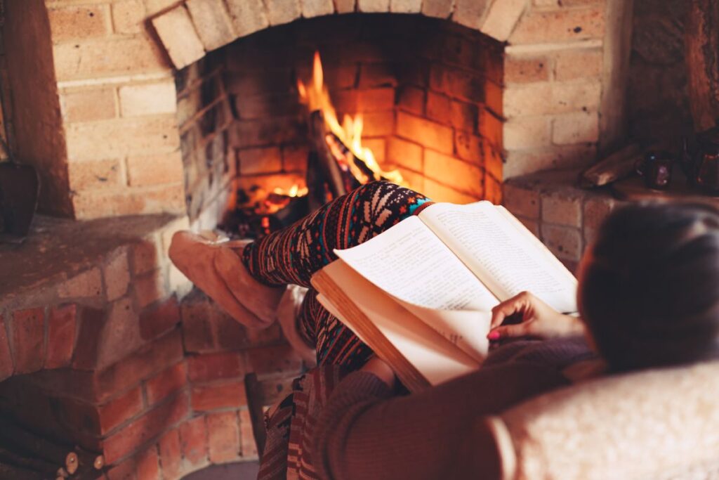 Person reading a book by the fireplace, wrapped in cozy winter warmth.