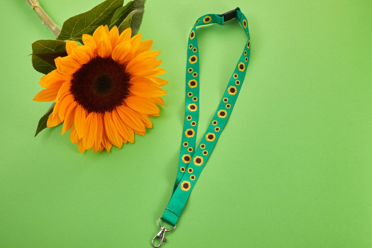 Hidden Disabilities Sunflower lanyard on a green background beside a bright sunflower.