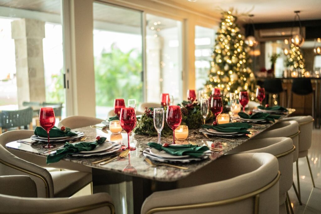 Festive holiday dinner table with red glasses, candles, and Christmas tree lights.