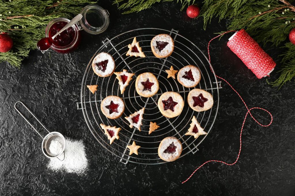 Christmas cookies with jam centers and powdered sugar on a cooling rack.