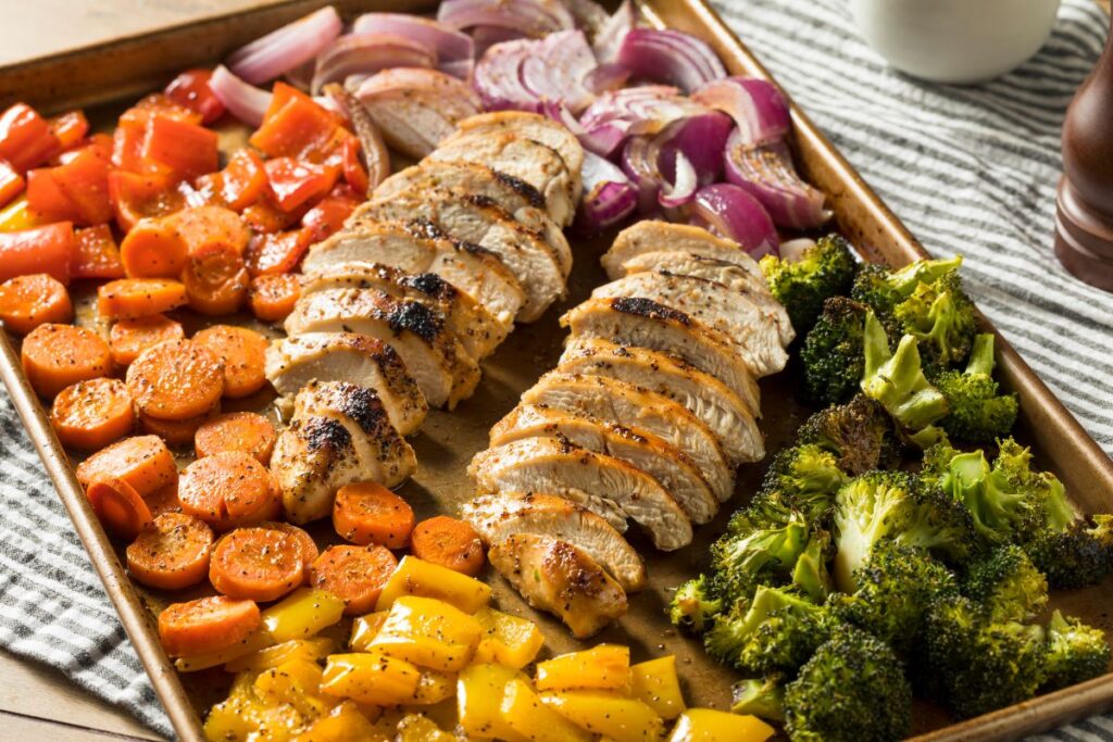 Sheet pan dinner with roasted chicken, broccoli, carrots, peppers, and onions.