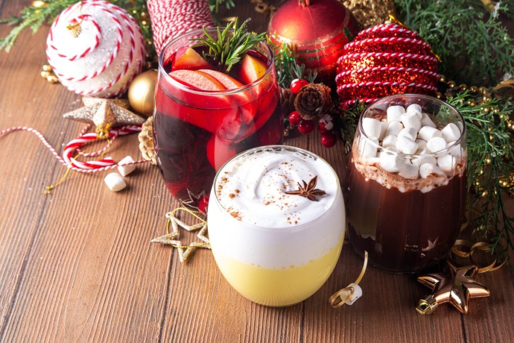 Holiday drink setup with hot cocoa, eggnog, mulled cider, and Christmas decorations.