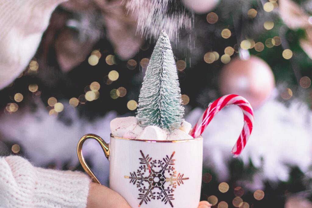 Holiday hot cocoa in a white mug with candy cane and Christmas tree decoration, dusted with powdered sugar snow.