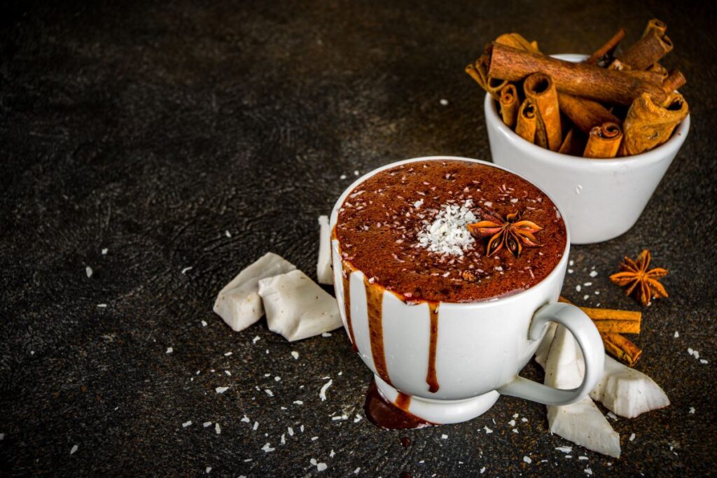 Dairy-free hot cocoa with coconut flakes, cinnamon sticks, and star anise garnish.