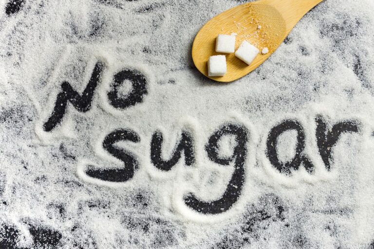 No sugar message written in white sugar with cubes on wooden spoon.