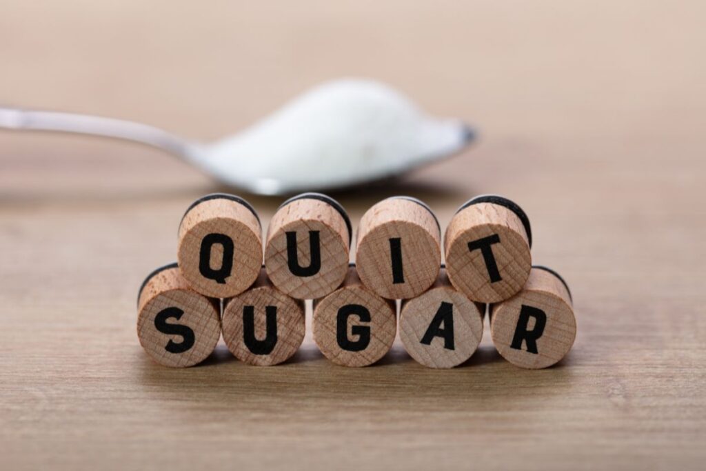 Wooden blocks spelling quit sugar with spoonful of sugar in background.