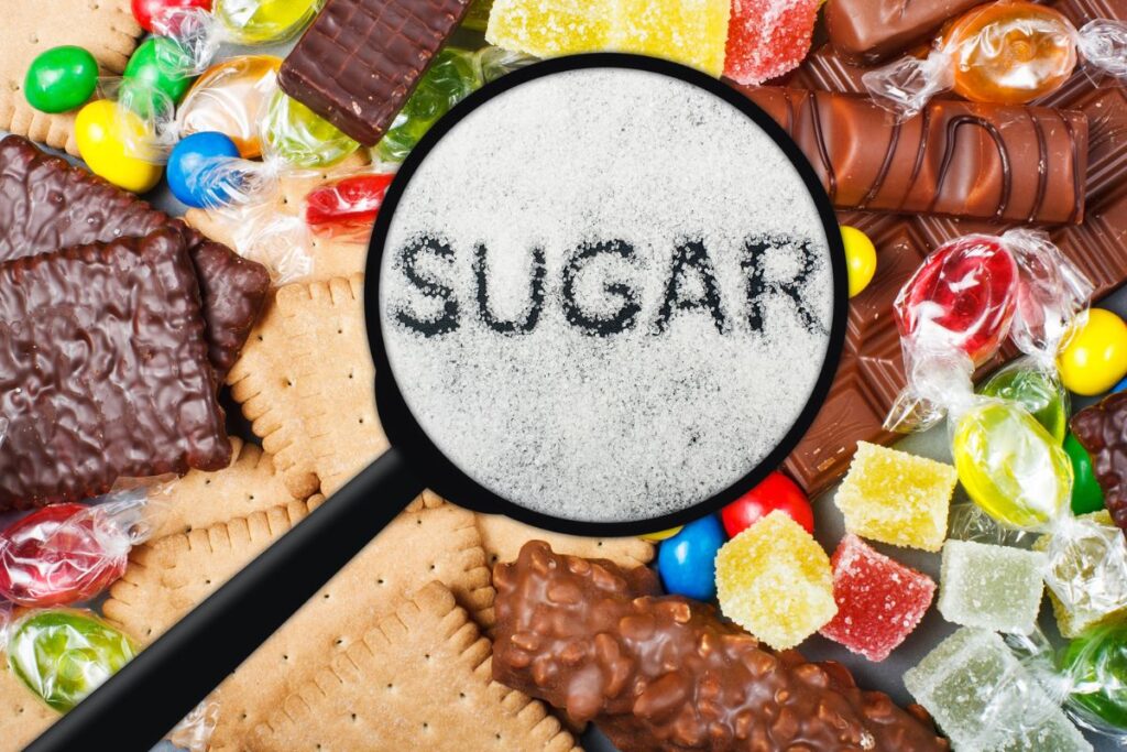 Magnifying glass showing sugar among candies, cookies, and chocolate bars.