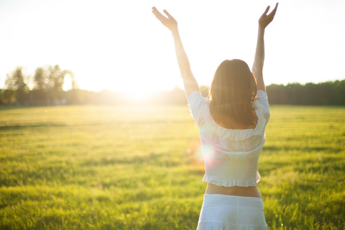 Woman raising arms in sunlight over a grassy field, symbolizing natural ways to get dopamine and happiness.