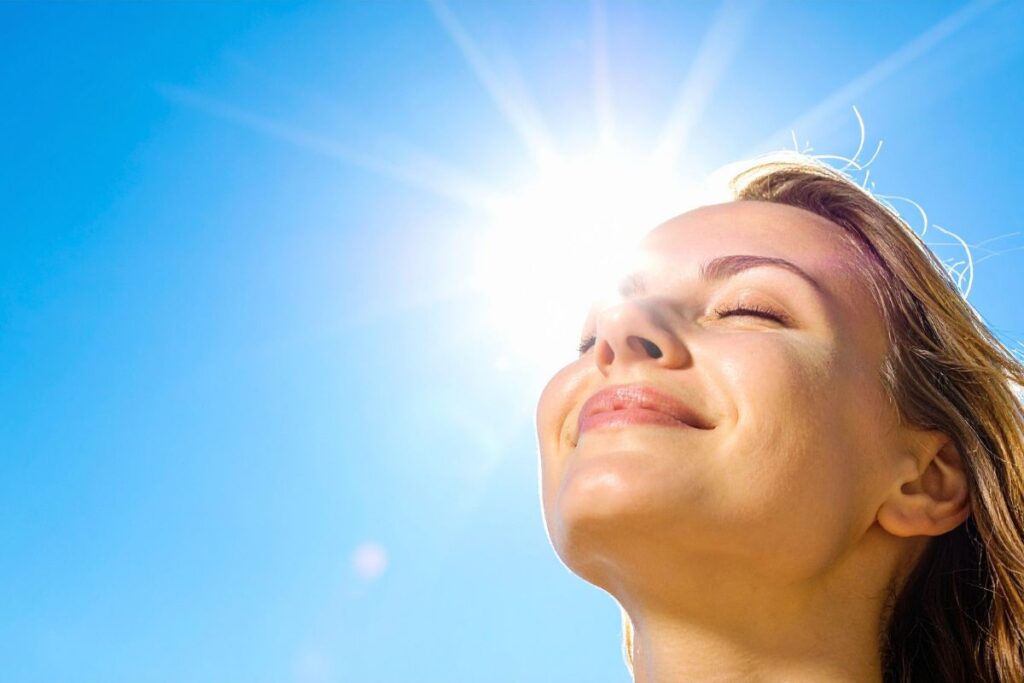 Smiling woman enjoying sunlight with eyes closed, showing how natural sun exposure boosts dopamine.