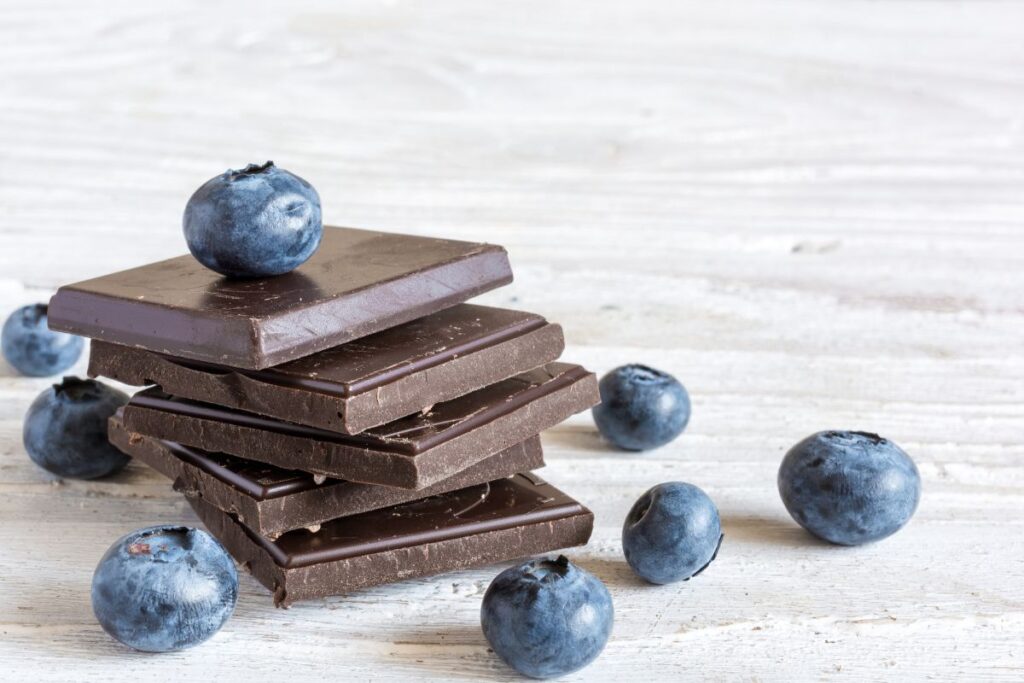 Stack of dark chocolate with fresh blueberries on a white board.