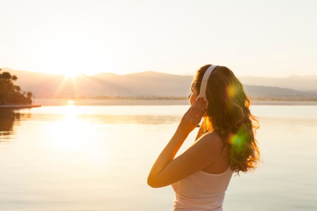 Woman wearing headphones outdoors at sunset, listening to music as a dopamine booster.