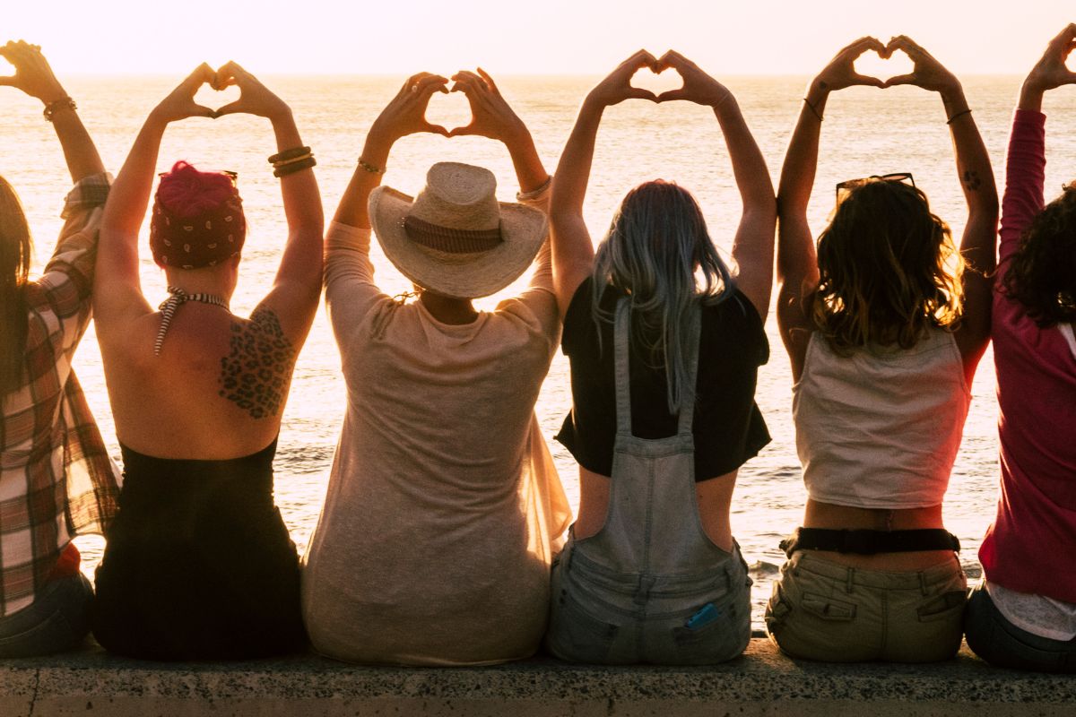 Group of women making heart shapes with their hands at sunset, symbolizing love and connection.