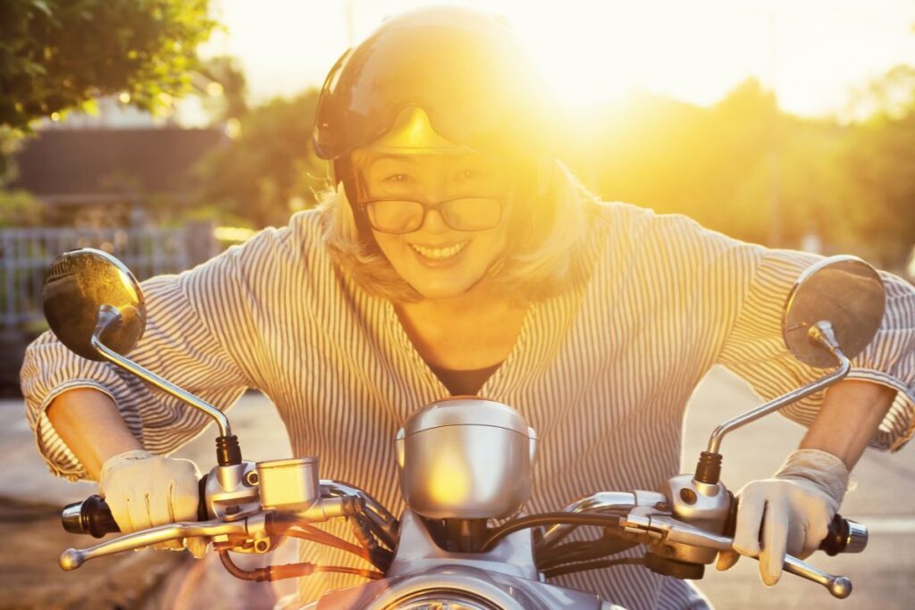 Smiling older woman riding a scooter at sunset, radiating energy and joy in later life.