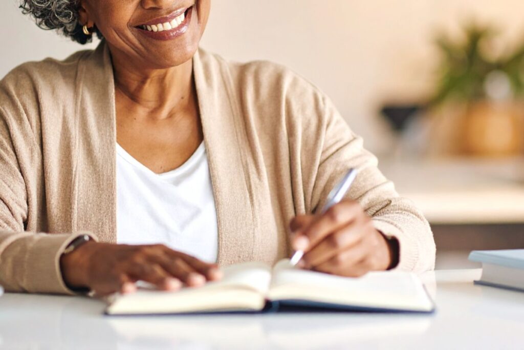 Close-up of a woman writing in a journal and smiling, symbolizing self-reflection and confidence.