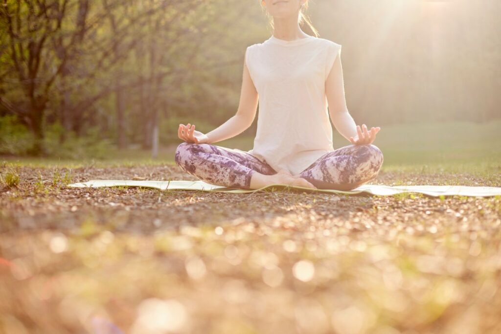 Woman meditating cross-legged on a yoga mat in nature, focusing on calm and mindfulness.