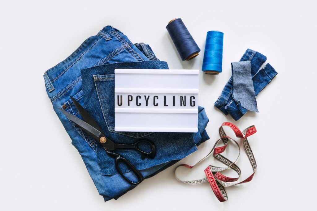 Upcycling setup with jeans, scissors, sewing thread, and tape for budget-friendly slow fashion.