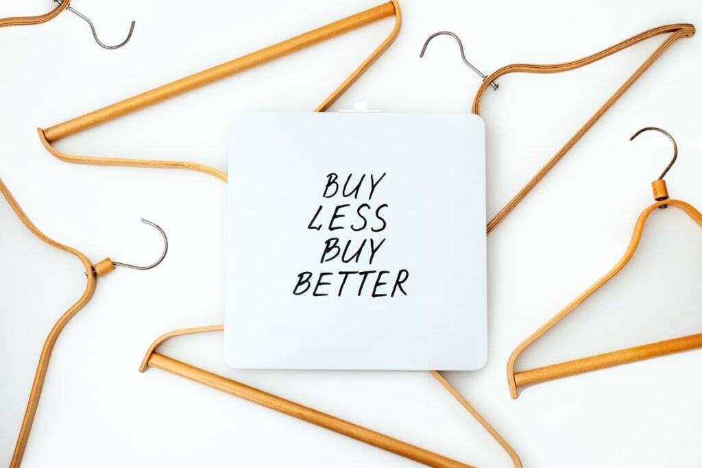 Buy less buy better message surrounded by wooden hangers on white background.