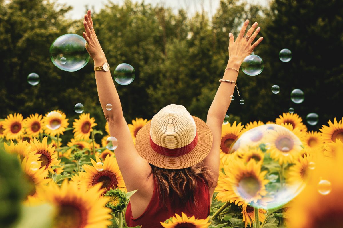 Woman with hat raising arms in a sunflower field enjoying sunshine.