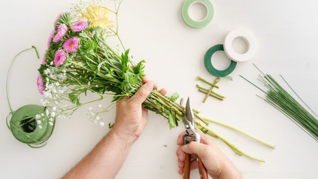 Hands trimming flower stems with pruning shears to prepare a fresh bouquet.