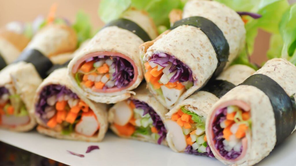 Platter of colorful vegetable rolls filled with carrots, cabbage, and lettuce wrapped in bread slices.