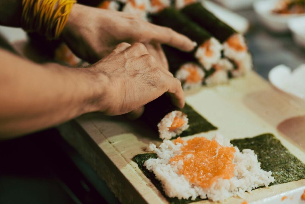 Chef’s hands rolling fresh sushi filled with rice and salmon.